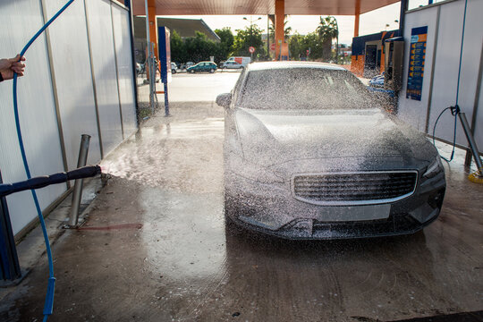 Car cleaning at a gas station by spraying foam on the vehicle with a sprayer gun.