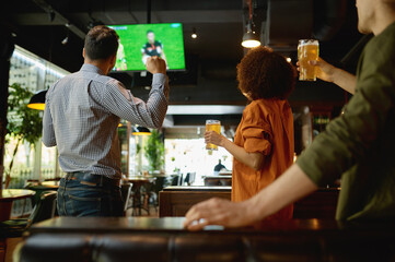 Group of friends watching football match on tv screen at sport bar