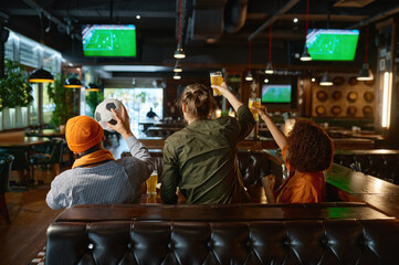 Group of young friends watching football on tv screen at sports bar