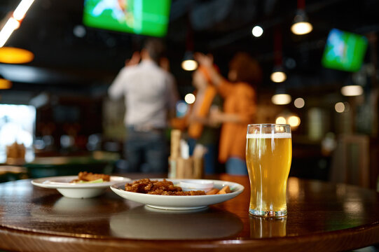 Beer glass and fast food snack on table in sports bar