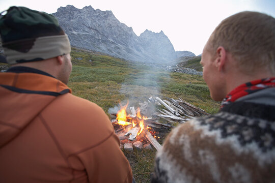 2 male friends sitting at a camp fire in Greenland