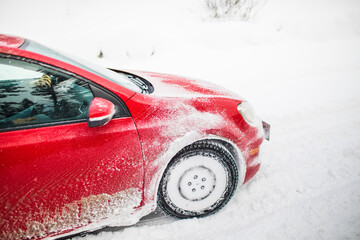 Side view of red car driving through snow storm.