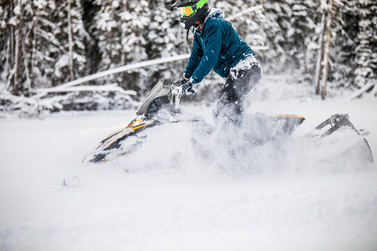 Side view of man snowmobiling through deep snow.