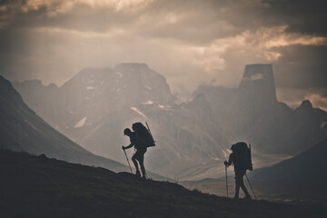 Silhouette of two backpackers hiking with rugged mountain view.
