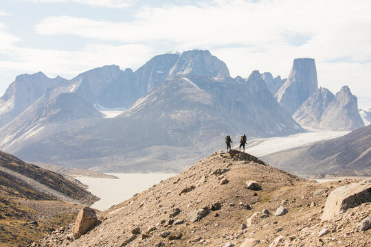Two hikers stand on high mountain ridge in Akshayak Pass Baffin Island