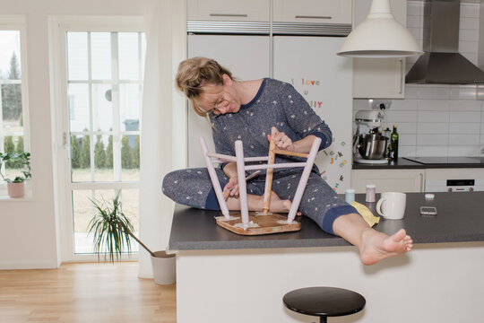 woman sat at home painting a stool in the kitchen