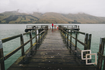 Woman on a red jacket standing at Port Levy Jetty, Banks Peninsula, NZ