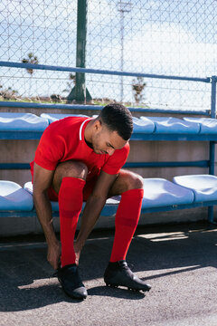 African American male soccer player sitting and fixing boots on bench
