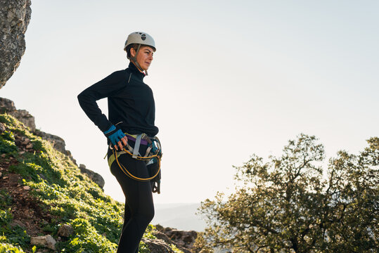 Concept: adventure. Female climber with helmet and harness. Thoughtful standing on a rock on top of the mountain. Solar luminous flare. Via ferrata in the mountains.
