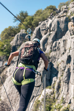 Concept: adventure. Woman with helmet, harness and backpack. Walking over the abyss over a monkey bridge. doing via ferrata in the mountains.