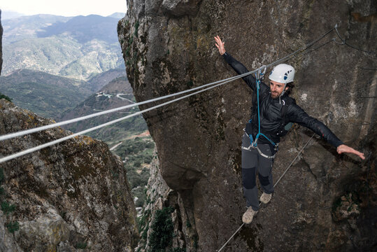 Concept: Adventure. Climber Man With Helmet And Harness. Balancing Assured On A Tibetan Cable Bridge. Climbing To The Top Of The Mountain. Via Ferrata On Rock.