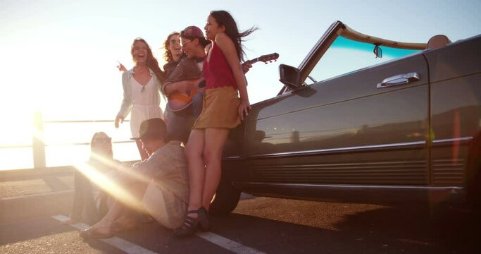 Hipster friends celebrating a sunset at the beach with an acoustic guitar during a summer road trip