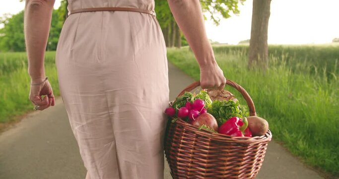 Cropped rearview image of a woman holding a woven basket full of fresh organic vegetables