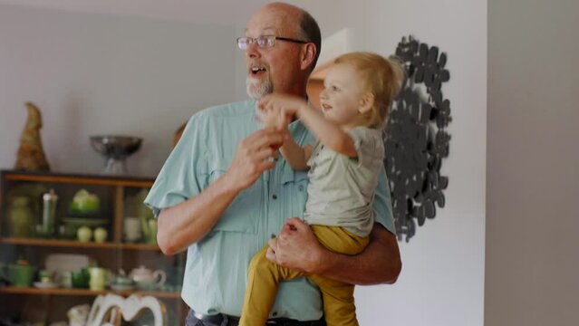 Handheld shot of happy grandfather carrying grandson while dancing at home