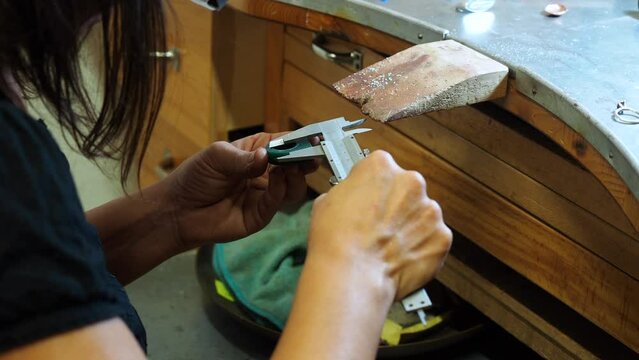 Handheld shot of female jeweller using caliper while measuring wax in workshop