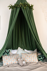 Bed decor in white and green tones, with a green canopy, pillows, a blanket and a children's toy.