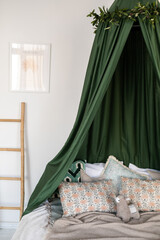 Bed decor in white and green tones, with a green canopy, pillows, a blanket, a children's toy and a picture on a white wall and a bamboo ladder.