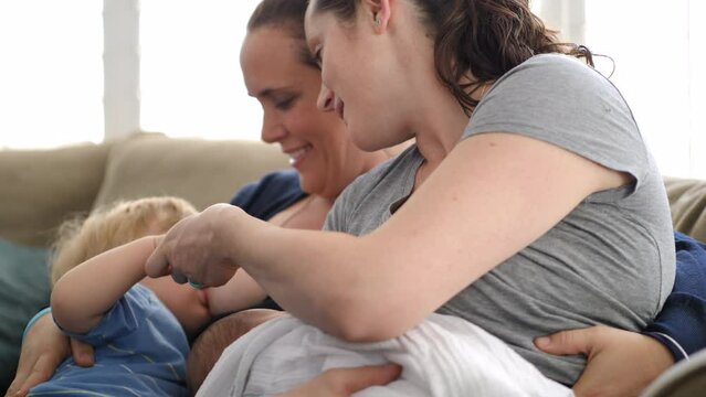 Tilt shot of lesbian mothers breastfeeding sons while sitting on sofa at home
