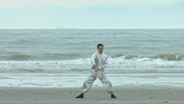Practicing kung-fu, chinese man in kimono on beach.