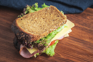 Sandwich with a ham, cheese, tomato, salad lettuce on a wooden board