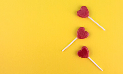 Three pink candies on stick in shape of a heart on yellow background