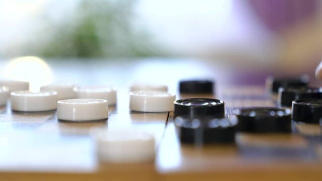 Boy's hand moves a white piece of checkers. Child playing checkers with granny.