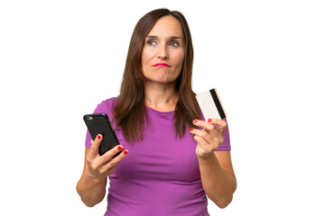 Naklejka premium Middle-aged caucasian woman over isolated background buying with the mobile with a credit card while thinking