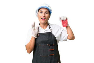 Butcher woman wearing an apron and serving fresh cut meat over isolated background with surprise and shocked facial expression