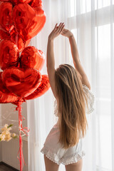 Beautiful young girl at home in bedroom in the morning enjoy valentines day celebration with heart shaped balloons