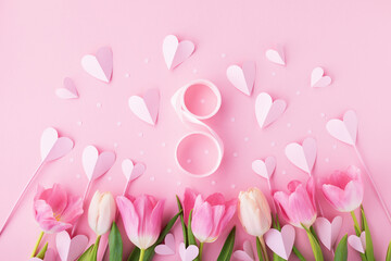 Spring greeting card for 8 March with bouquet of tulip flowers and paper hearts on pastel pink table top view. Flat lay.