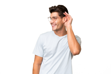 Young caucasian handsome man over isolated background listening to something by putting hand on the ear