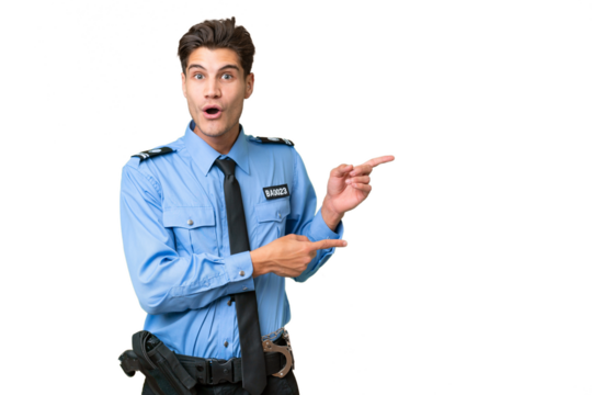 Young police man over isolated background surprised and pointing side
