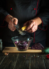 The chef adds cheese to a fresh red cabbage salad in a restaurant kitchen. Cooking healthy or vegetarian food. Copy space