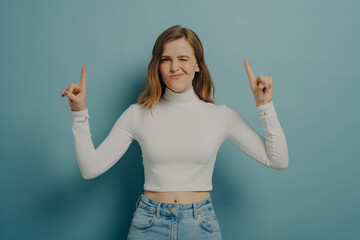 Millennial girl pointing indicating with forefingers upwards and winking at camera