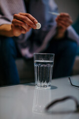 Close-up of the man taking medicine, putting Aspirin paracetamol pill splashing into a glass of water.