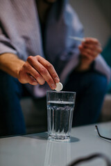 Close-up of the sick man putting aspirin paracetamol pill splashing into a glass of water.