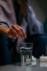 Close-up of the man's hand putting aspirin paracetamol pill splashing into a glass of water.