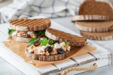Sandwich with baked fish (tuna or salmon) with black olives, Feta cheese and parsley on rye bread. Mediterranean seafood breakfast.   Selective focus - 570847906