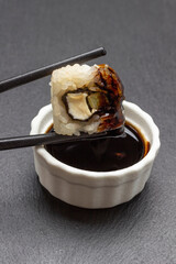 Chopsticks hold sushi over a bowl of soy sauce.