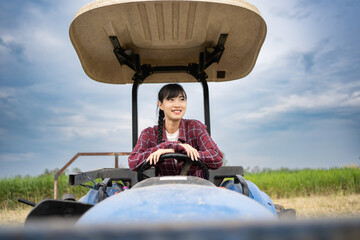 Portrait of young adult Asian woman farmer sitting in tractor smiling to work. Field farming vehicle. Machine for agriculture.
