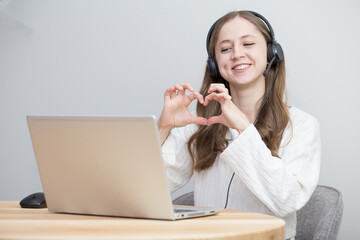 beautiful girl communicates with her lover through a laptop and shows a heart
