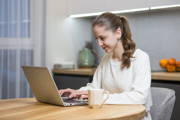 beautiful girl works at home with a laptop at the table and smiles