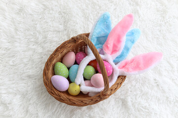 Top view of beautiful colorful Easter eggs and bunny rabbit ears headband in wicker basket on...