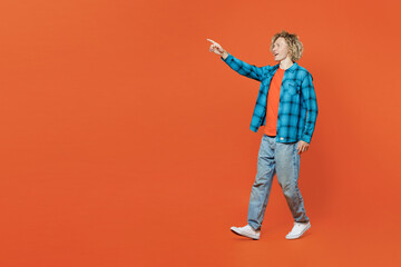 Full body young happy blond caucasian man wear blue shirt orange t-shirt point index finger aside on workspace area mock up isolated on plain red background studio portrait. People lifestyle concept.