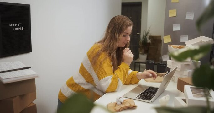 Entrepreneur female started her small business just in her apartment at home, woman works on a laptop in the kitchen among boxes with goods