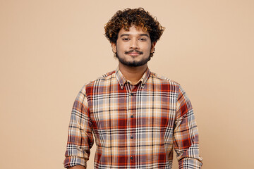 Confident satisfied cool student Indian man wearing checkered brown shirt casual clothes looking camera isolated on plain pastel light beige color background studio portrait. People lifestyle concept.