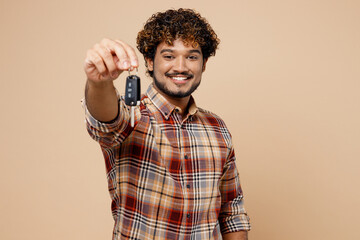 Young smiling happy Indian man wear brown shirt casual clothes hold in hand giving car keys fob keyless system isolated on plain pastel light beige background studio portrait People lifestyle concept