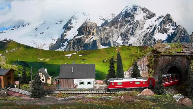 Florence, Italy January 2022: Miniature red train. Model railway. Red model toy train comes out of the tunnel with snowed mountains setting in the background