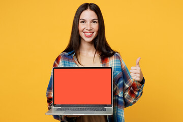 Young cheerful fun smart smiling IT woman wearing blue shirt beige t-shirt holding use working on laptop pc computer with blank screen workspace area show thumb up isolated on plain yellow background.