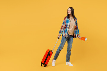 Full body traveler woman wear casual clothes hold valise passport ticket look aside isolated on plain yellow background Tourist travel abroad in free time rest getaway Air flight trip journey concept